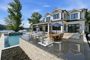A modern house with a swimming pool, outdoor seating, and a view of a lake.