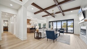 Amplia sala de estar con techo alto, vigas de madera, chimenea y ventanas grandes que ofrecen vistas al exterior.