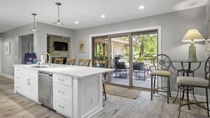 Eine geräumige Küche mit einer großen Kochinsel, ein Essbereich mit Außenmöbeln und Blick ins Freie.