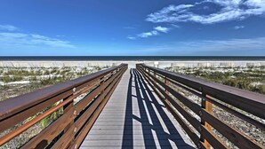 Ein Holzsteg führt zu einem Strand unter blauem Himmel.