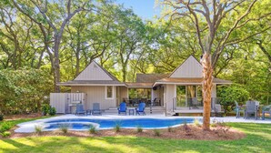 Ein zweistöckiges Haus mit überdachter Terrasse, Pool und Rasenfläche.