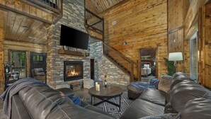 A cozy living room with a stone fireplace, leather sofas, and a staircase leading to an upper level.