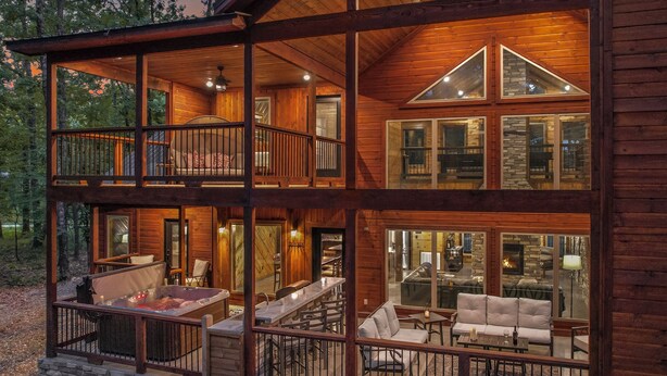 A two-story log cabin with a balcony, a hot tub, and a fireplace.