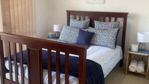Una camera da letto con una culla in legno, un letto con biancheria a motivi, un comodino con una lampada e una parete decorata.
