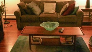 Una sala de estar con un sofá marrón, una mesa de centro de madera y un adorno en la pared.