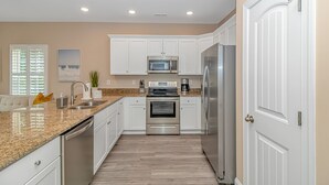 A modern kitchen with white cabinets, stainless steel appliances, granite countertops, and a wooden floor.