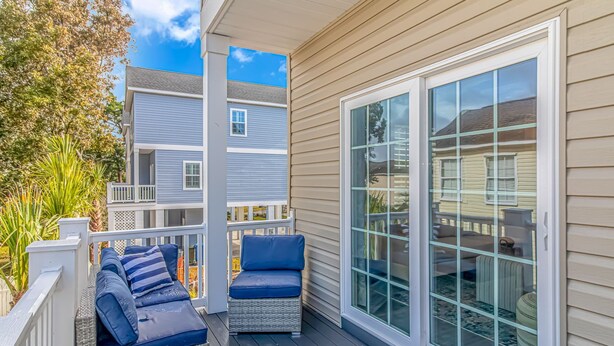A covered outdoor area with a sliding glass door, a wicker sofa with cushions, and a view of neighboring houses.