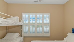 A room with bunk beds, a large window with blinds, and a bed.