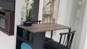 Een moderne eetruimte met een houten tafel en zwarte stoelen, een televisie aan de linkerkant en een decoratief kunstwerk boven de deur.