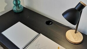 Un bureau avec un carnet, un stylo, une lampe et un vase rempli de fleurs.