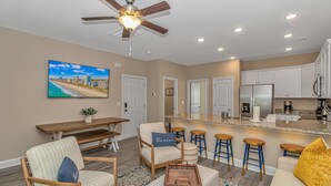 A modern living room with a dining area, kitchen, and a large window with a cityscape view. - PRIVATE HOT TUB, steps from the beach, boardwalk and many other attractions. (Myrtle Beach)