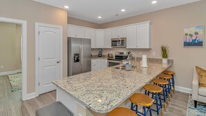 A modern kitchen with white cabinets, stainless steel appliances, a granite countertop, and bar stools. - PRIVATE HOT TUB, steps from the beach, boardwalk and many other attractions. (Myrtle Beach)