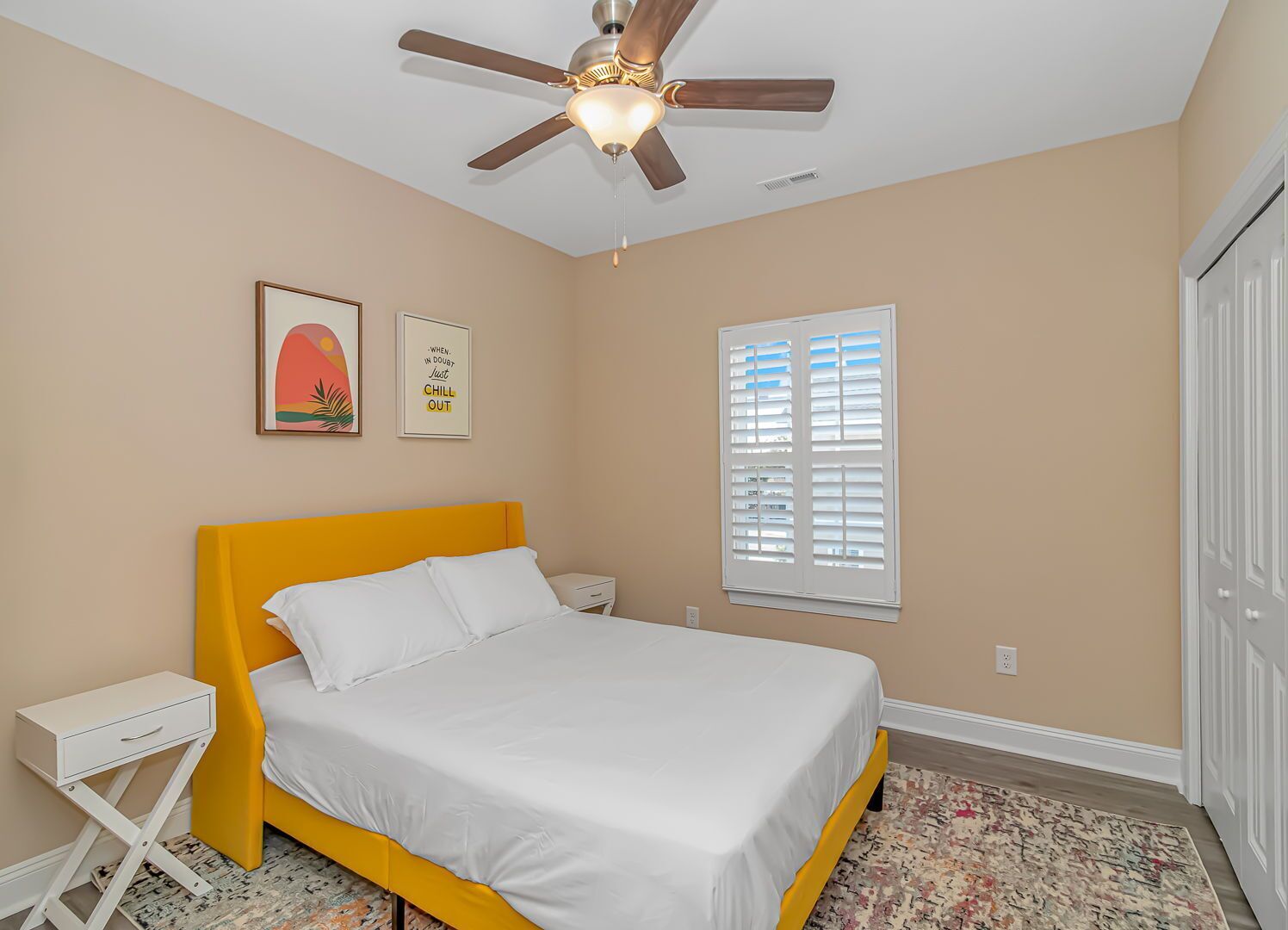 A bedroom with a bed, a ceiling fan, a window with blinds, and a door.