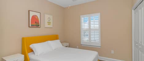 A bedroom with a bed, a ceiling fan, a window with blinds, and a door.