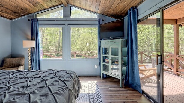 Ein Schlafzimmer mit einem großen Bett, einem Fernseher und Blick auf eine Holzterrasse.
