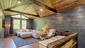 Ein gemütliches Blockhaus-Interieur mit einer Eckcouch, einem Ledersessel, einem kleinen Holztisch und einem Fenster, das für natürliches Licht sorgt.