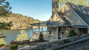 Une maison dotée d’une grande véranda donnant sur un lac, entourée d’arbres.