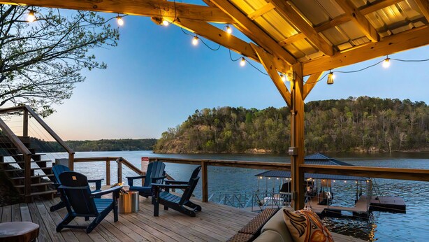 Une terrasse en bois avec des sièges extérieurs, donnant sur un lac avec une île boisée en arrière-plan.