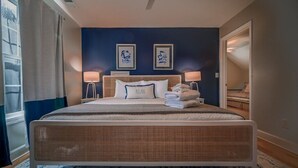 Un grand lit avec une tête de lit, deux lampes de chevet et un oreiller sur lequel est écrit le mot « RELAX ». Deux tableaux encadrés sont accrochés au mur au-dessus du lit.