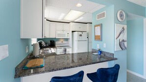 A modern kitchen with white cabinets, a granite countertop, and a central island with two blue chairs.