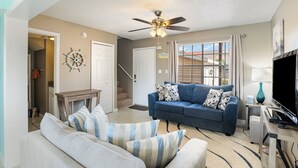 A living room with a blue sofa, a white sofa, a ceiling fan, and a TV.