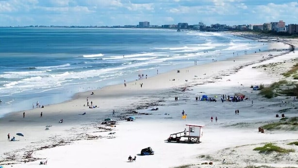 A beach with a lifeguard tower, sandy shore, and a pier in the background.
