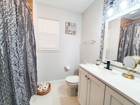 A bathroom with a toilet, a sink with a mirror, and a basket of toilet paper.
