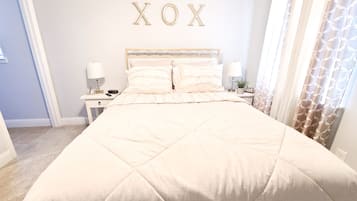 A neatly made bed with a quilted headboard, bedside tables with lamps, and a wall decoration spelling "XOX".