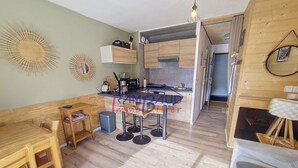 A compact kitchen with wooden cabinets, a dining table, and a bar stool. - Studio cabin   4 People  Resort center   Parking (VALLOIRE)