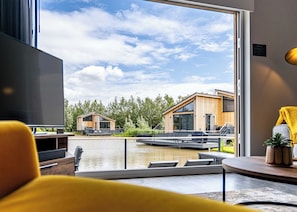 A modern interior with a large window overlooking a water body and two wooden buildings.