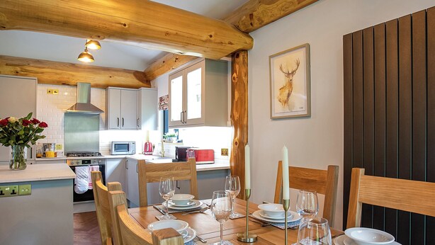 Ein Essbereich mit Holzkohlenstühlen und einem Tisch für vier Personen, eine Küche im Hintergrund und ein Bild eines Hirschkopfes im Rahmen an der Wand.