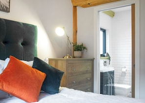 A bedroom with a bed, a dresser, a lamp, and a potted plant.
