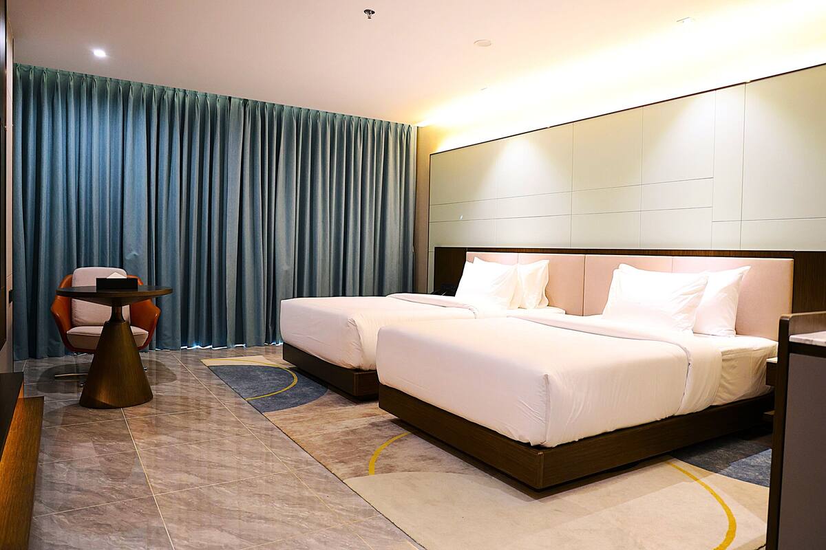 Habitación de hotel con dos camas, una mesa redonda y una silla.