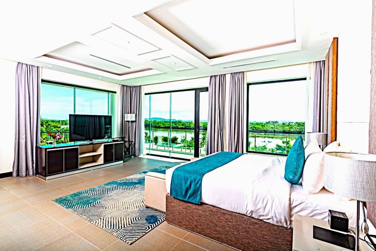 Habitación de hotel moderna con una cama grande, televisión y balcón con vistas a zonas verdes.