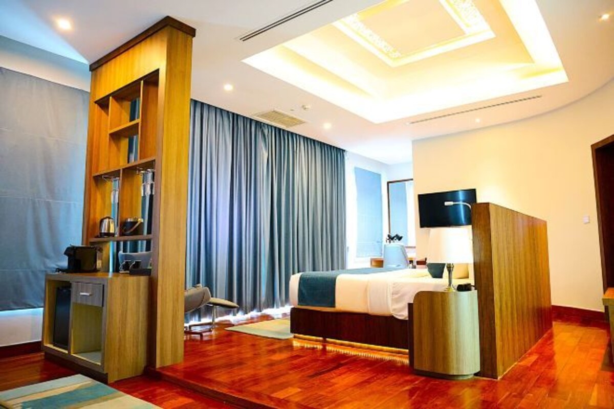 A modern hotel room with a wooden wardrobe, a bed, a desk, and a large window with curtains.