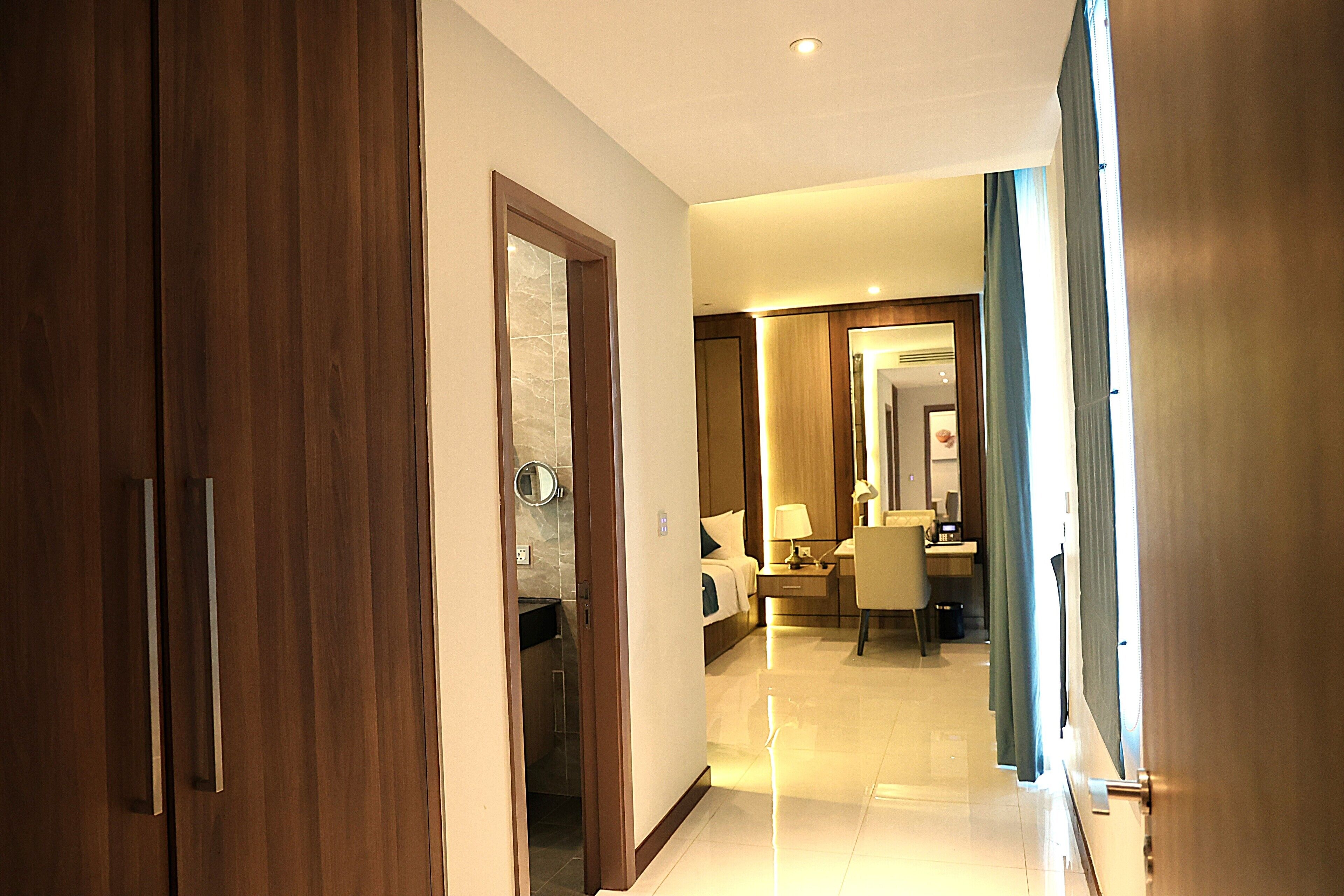 A hotel corridor with wooden doors, a bed, a desk, and a mirror.