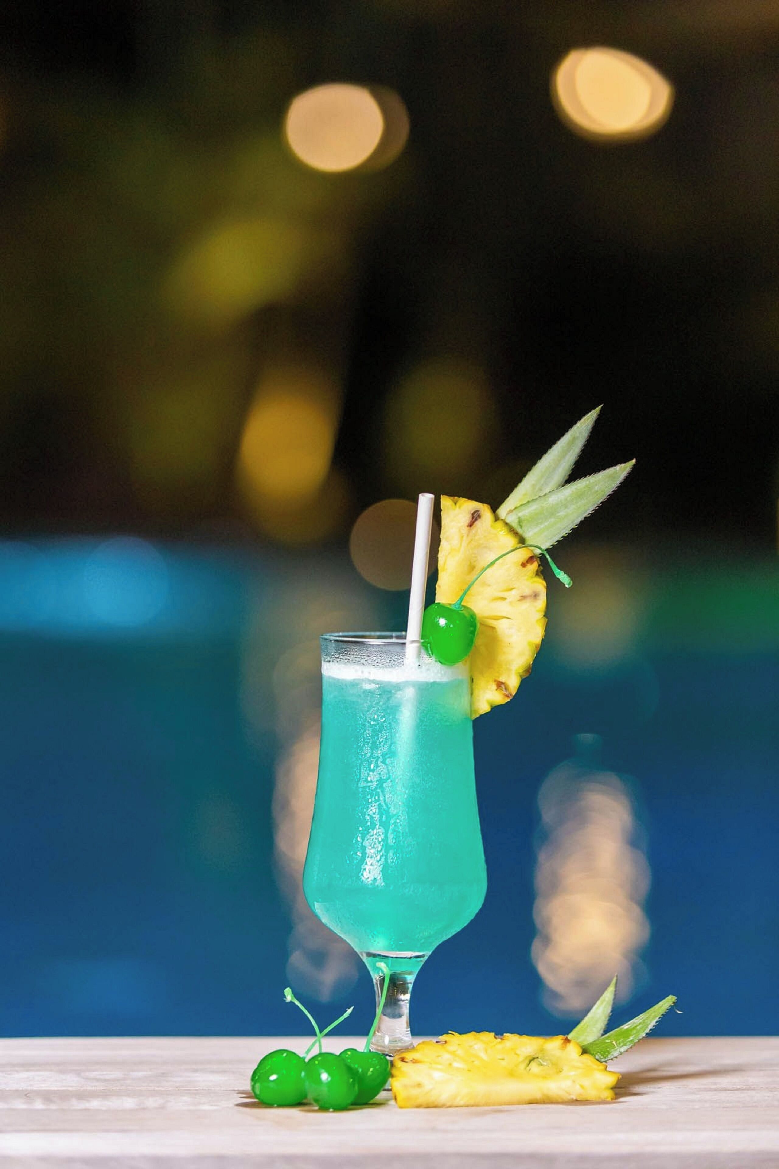 A cocktail with a straw, pineapple slice, and cherry garnish on a table.
