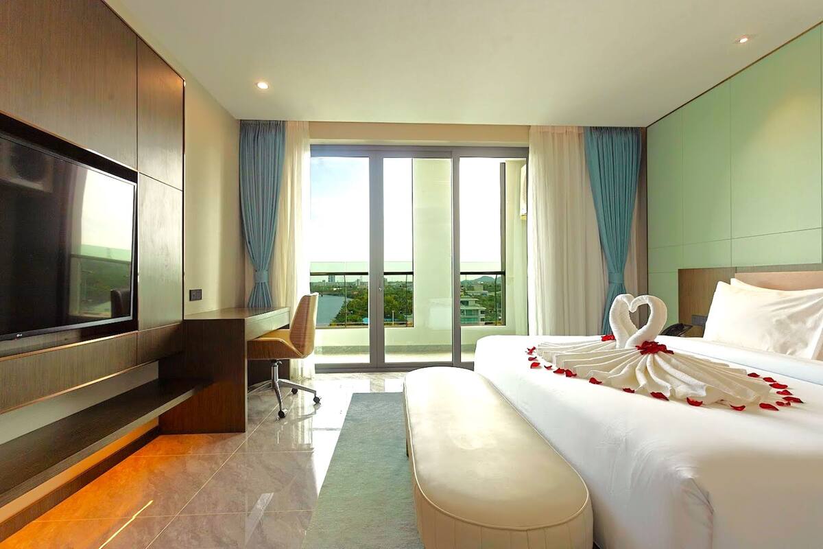 Habitación de hotel moderna con una cama grande, un televisor de pantalla plana, un escritorio y vistas de la ciudad a través de las puertas del balcón.