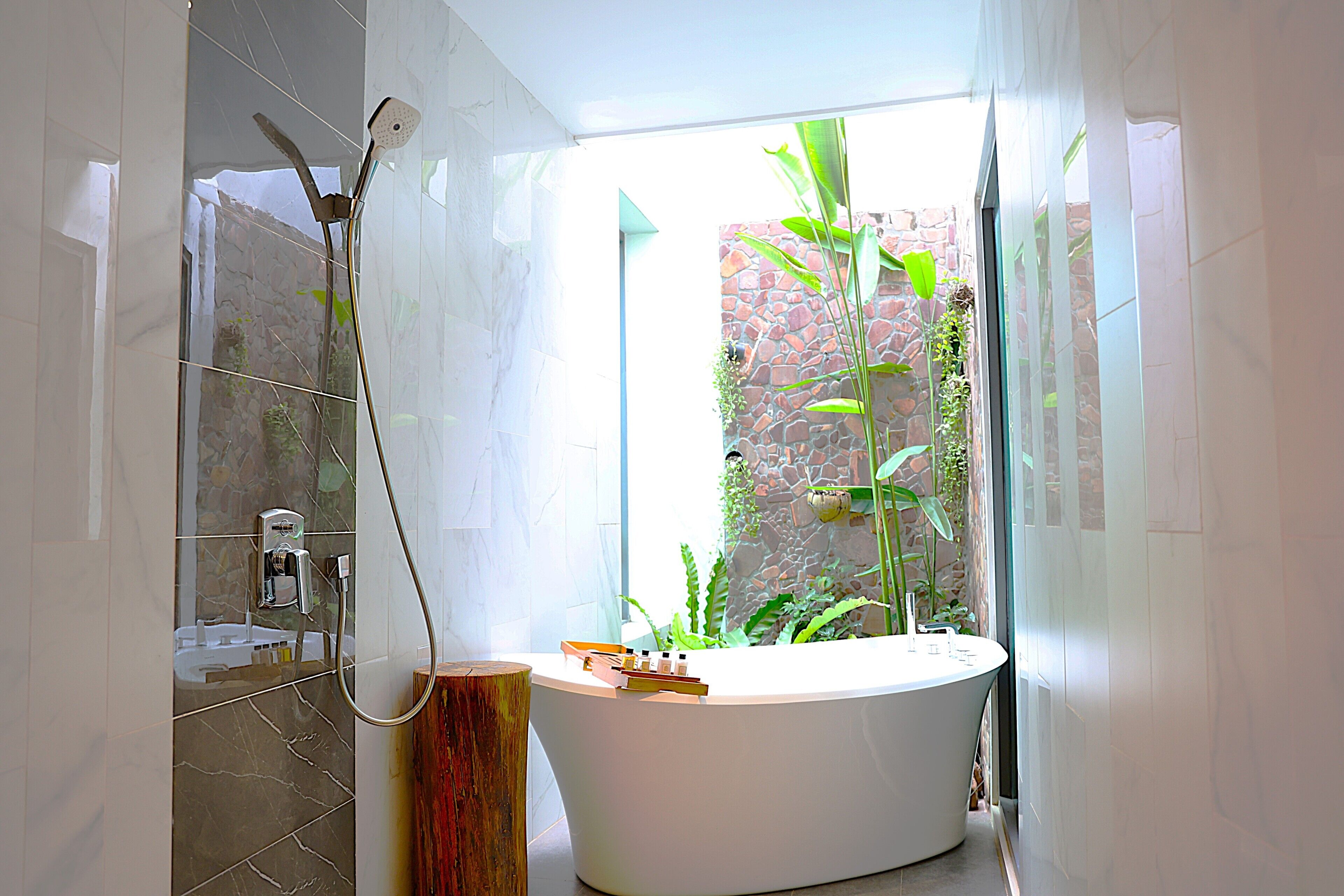A modern bathroom with a freestanding bathtub, a showerhead, and a view of a garden through a glass door.
