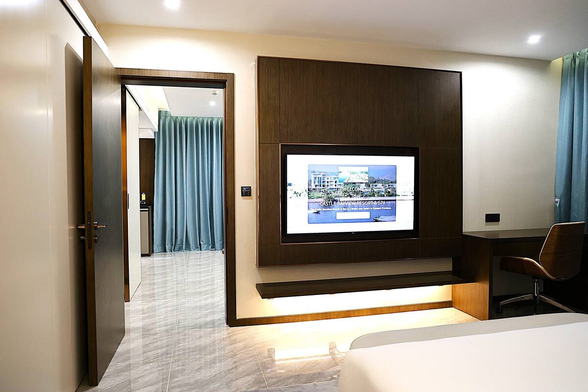 Habitación de hotel con televisión montada en la pared, un escritorio y una silla.