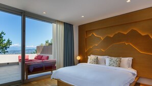 Une chambre moderne avec un grand lit, une vue dégagée sur le paysage grâce à une porte-fenêtre coulissante, et une tête de lit en bois ornée d’un motif de montagne.