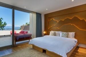 Quarto moderno com uma cama grande, vista através de uma porta de correr e cabeceira de madeira com desenho de montanhas.