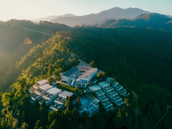 An aerial view of a residential area with modern houses, surrounded by dense forest and hills.