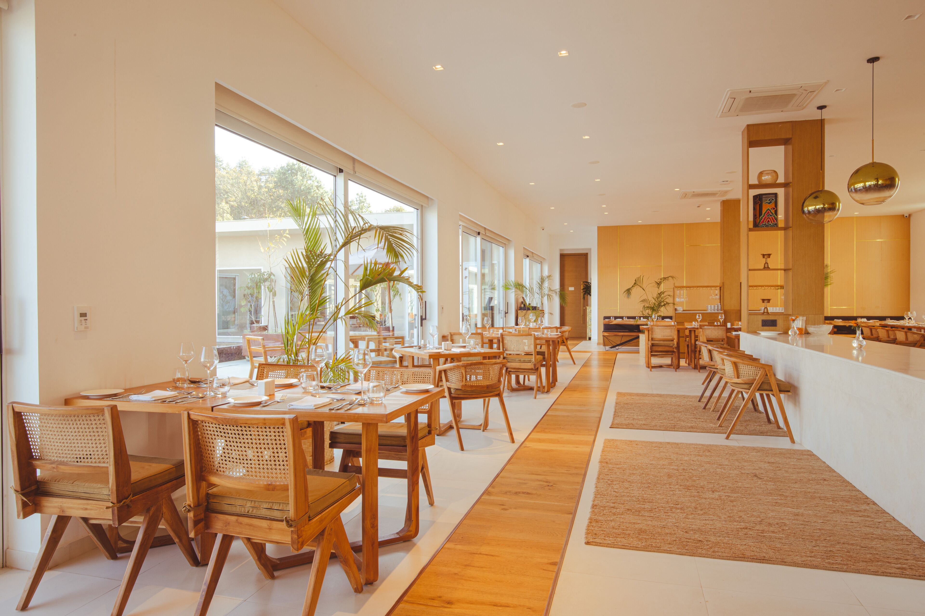A spacious dining area with wooden tables and chairs, large windows, and a kitchen in the background.