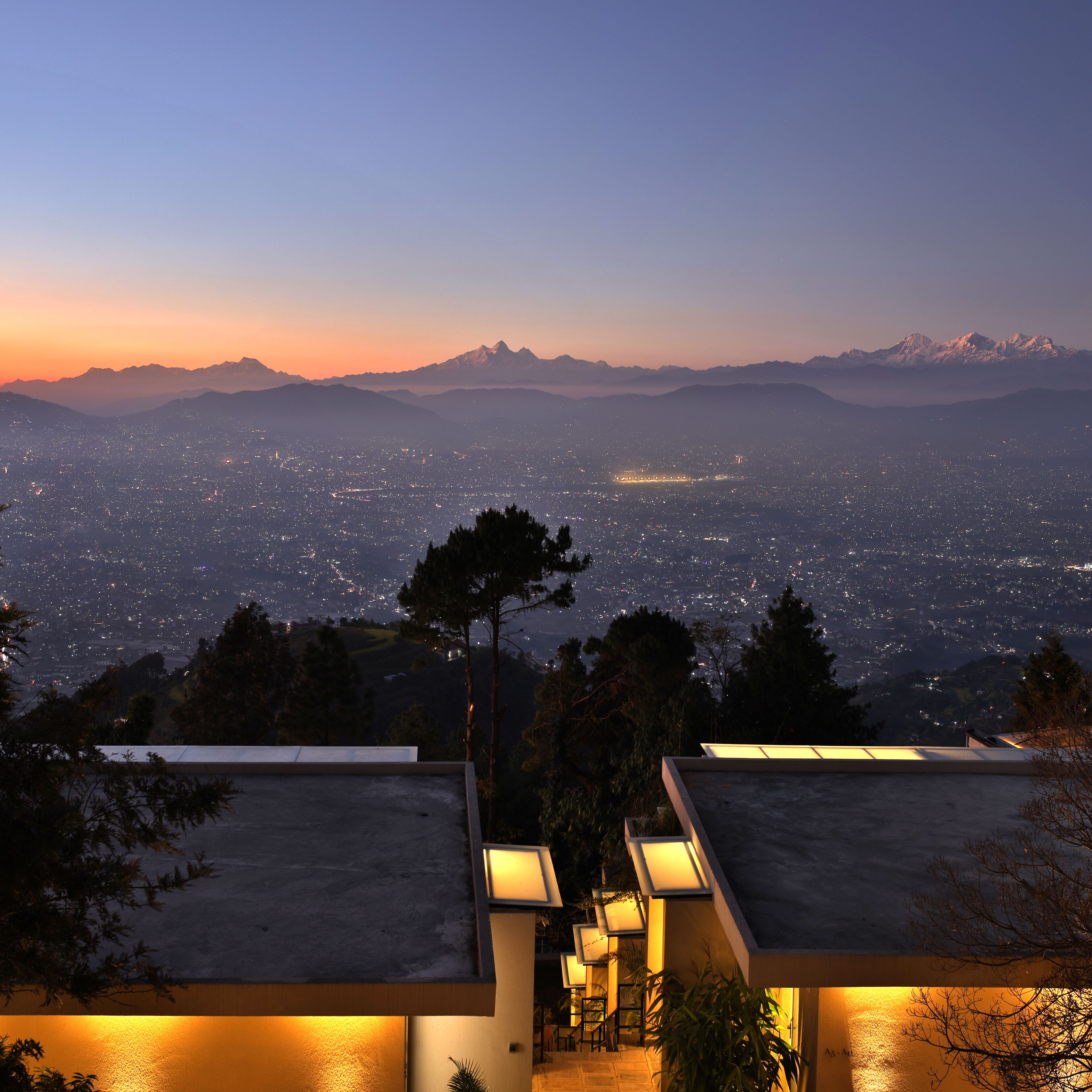 A rooftop terrace with a panoramic view of a city at dusk, overlooking a mountain range.