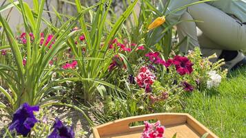 Iemand knielt op het gras en verzorgt een tuin met verschillende bloemen en planten.