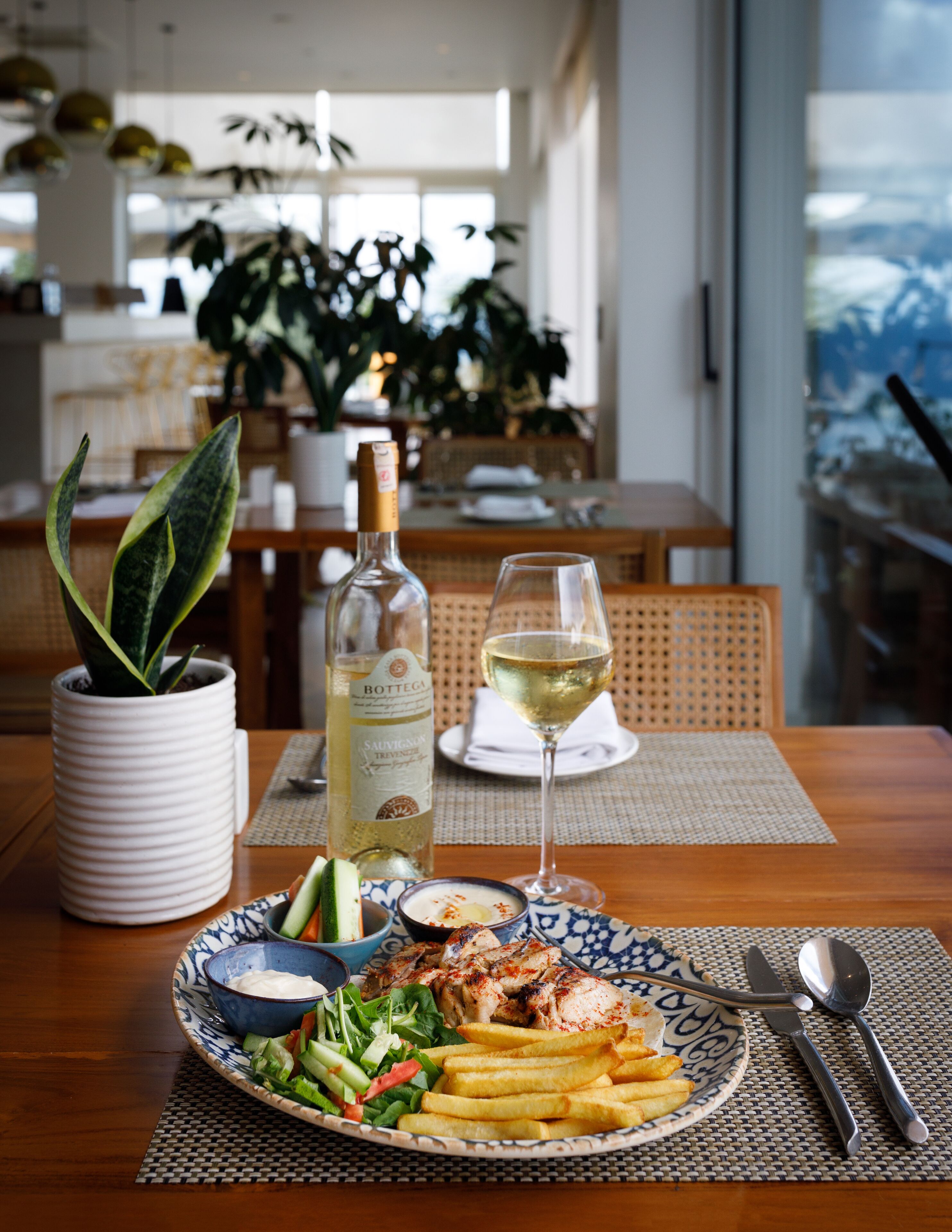 Una mesa de comedor con un plato de comida, una botella de vino y una copa de vino.