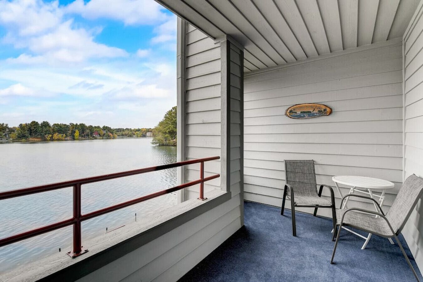 A balcony with a view of a lake, a small table, and two chairs.