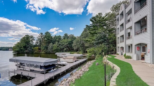 A waterfront property with a dock, a grassy area, and a building with balconies. - Lakefront Luxury 212 · Lakefront Luxury for Families or Couples (Wisconsin Dells)
