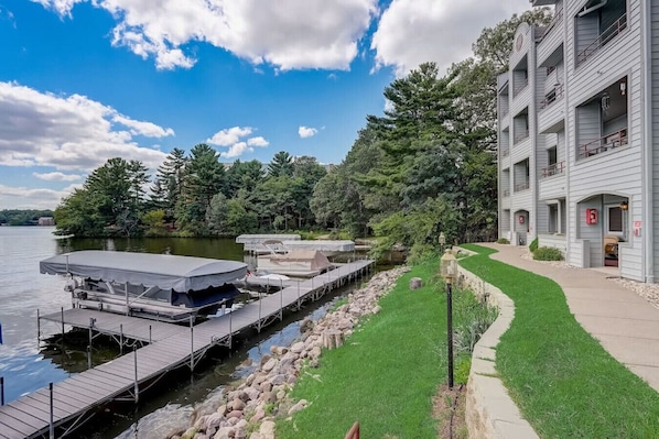 A waterfront property with a dock, a grassy area, and a building with balconies.